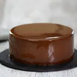 Gâteau rond avec un glaçage chocolat miroir brillant, posé sur une assiette ardoise.