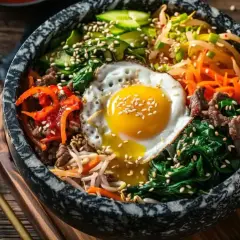 Un bol de bibimbap coloré avec œuf au plat, bœuf, légumes et riz. Une invitation à essayer cette recette !