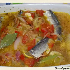 Sardines à l'escabèche dans un plat blanc, avec des tomates, oignons, citron et feuilles de laurier.