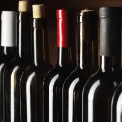Une rangée de bouteilles de vin rouge, certaines avec des capsules de différentes couleurs, pour vous aider à comment reconnaître un bon vin rouge.