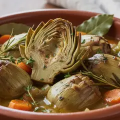 Artichauts barigoule mijotés dans un plat en terre cuite avec carottes, herbes et bouillon. Une recette savoureuse et colorée.