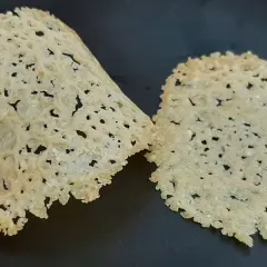 Deux tuiles de parmesan croustillantes et ajourées, posées sur une surface sombre.