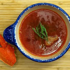 Une délicieuse bisque de homard, garnie d'herbes fraîches, est servie dans un bol bleu et blanc, accompagnée d'une pince de homard sur une planche en bois.