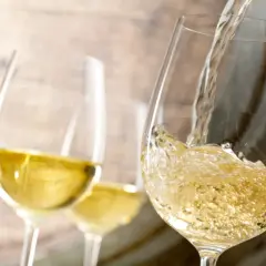 Le vin blanc est versé dans un verre, rappelant le processus de vinification. Deux autres verres sont visibles en arrière-plan.