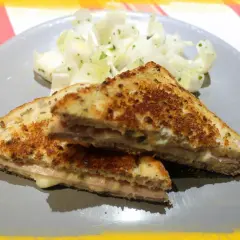 Un délicieux croque monsieur à la poêle, doré et garni de jambon et fromage fondant, servi avec une salade fraîche.