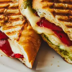 Un délicieux sandwich italien grillé, garni de fromage fondant, de poivrons rouges et de pesto vert.