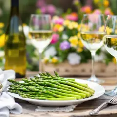 Un plateau d'asperges chaudes attend d'être dégusté avec un verre de vin blanc, dans un cadre floral lumineux.
