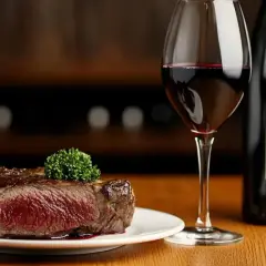 Un savoureux steak de vin cœur de bœuf, garni d'une touche de verdure, accompagné d'un verre de vin rouge et d'une bouteille.