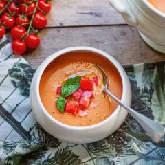 Un bol de soupe à la tomate fraîchement préparée, garnie de dés de tomates et de basilic. Des tomates cerises fraîches sont disposées à côté.