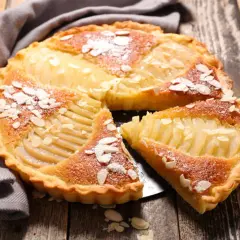 Une délicieuse tarte au poire, garnie d'amandes effilées et saupoudrée de sucre glace, repose sur un plateau en bois.