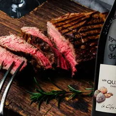 Un steak grillé et tranché sur une planche en bois, accompagné d'une bouteille de vin rouge passe partout.