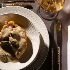 Un plat de poulet au vin jaune, crémeux et garni de morilles, servi sur une assiette texturée. Une table dressée avec élégance.