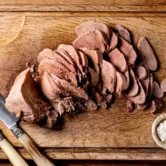 Tranché, la langue de bœuf attend d'être dégustée avec une sauce piquante et des cornichons. Un couteau et une fourchette sont prêts.