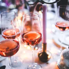 Verres remplis de bon vin rose, prêts pour une célébration festive avec des bougies et des lumières douces.