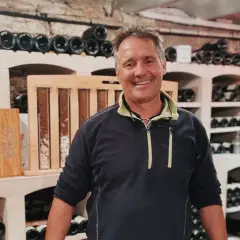 Bruno Clavelier, vigneron souriant, pose dans sa cave remplie de bouteilles.