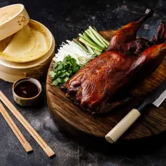 Un canard laqué prêt à être dégusté, accompagné de ses crêpes, sauce, légumes croquants et coriandre. Une recette parfaite pour un repas festif.