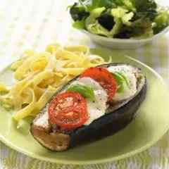 Aubergine farcie de mozzarella, tomates et basilic, servie avec des pâtes et une salade verte. Un plat savoureux et coloré.