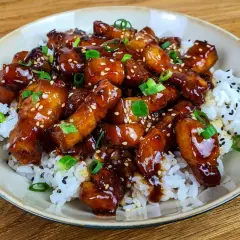 Un plat appétissant de porc au caramel asiatique, garni de graines de sésame et d'oignons verts, servi sur du riz blanc. Une recette à essayer !