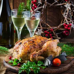 Un chapon rôti, prêt à être dégusté, avec deux verres de vin blanc et une décoration festive. Quel vin avec du chapon pour ce repas de fête ?