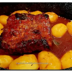 Un rôti de porc à la cocotte en sauce, doré et savoureux, mijote avec des pommes de terre fondantes. Un plat réconfortant prêt à être dégusté.