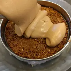 Une crème onctueuse est versée sur une base croustillante praliné feuilletine dans un cercle à pâtisserie.
