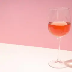 Un verre de rosé de macération, d'une belle couleur orangée, sur un fond rose et blanc.