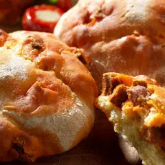 Gros plan sur des pains au chorizo dorés et croustillants, certains entiers, un autre coupé révélant la garniture savoureuse.