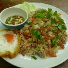 Un plat de riz thaï savoureux avec un œuf au plat, des tranches de concombre et une sauce piquante.