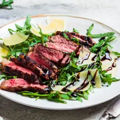 Une assiette de tagliata de boeuf, roquette, copeaux de parmesan et filet de vinaigre balsamique.