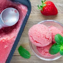 Un délicieux parfait glacé à la fraise, servi dans un bol avec des feuilles de menthe fraîche et des fraises entières.