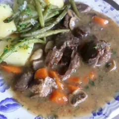 Un plat de civet de daim, avec des morceaux de viande tendres, des carottes, des champignons et des haricots verts, accompagné de pommes de terre.