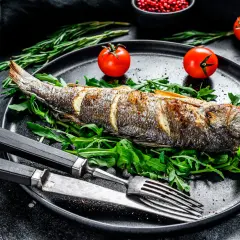 Bar au barbecue, entier et doré, servi sur un lit de roquette avec des tomates cerises et des herbes. Un délice à savourer !