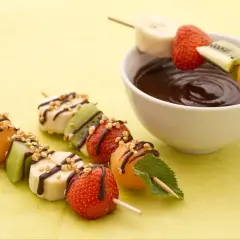 Délicieuses brochettes de fruits, bananes, fraises, kiwis et melons, arrosées de chocolat et de noix, prêtes à être trempées.