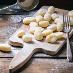 Gnocchis faits maison, prêts pour la cuisson. Une fourchette et une passoire à farine sur une planche en bois saupoudrée de farine, parfaits pour une recette de gnocchi.