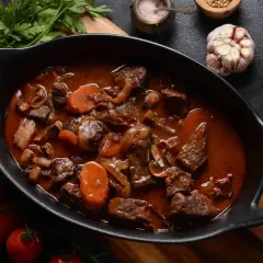 Un plat mijoté de bœuf bourguignon traditionnel, avec des carottes, des oignons et des champignons, prêt à être dégusté.
