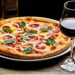 Une pizza garnie d'oignons et de pepperoni, accompagnée d'un verre de vin rouge. La question est : quel vin avec pizza ?