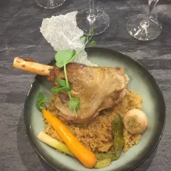 Souris d'agneau braisée au vin, servie sur un lit de couscous avec carottes et navets. Un plat savoureux et réconfortant.