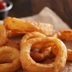Un tas d'oignon rings dorés et croustillants, servis sur du papier brun, avec un petit bol de ketchup en arrière-plan.