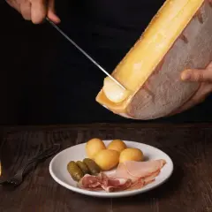 Un verre de vin blanc, parfait pour accompagner la raclette. Sur l'assiette, pommes de terre, cornichons et charcuterie.