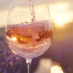 Verre de vin blanc rosé, pétillant, versé au coucher du soleil dans un champ de lavande. Douceur et légèreté, sans tanin.