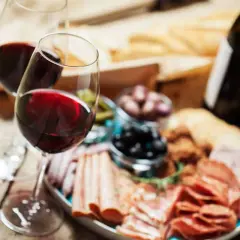 Deux verres de vin rouge, une bouteille, une assiette de charcuterie variée, olives et cornichons. Parfait pour savoir quel vin avec charcuterie.