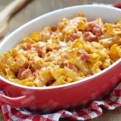 Un plat de gratin de pâtes au jambon, doré et gratiné, servi dans un plat rouge sur une serviette à carreaux.