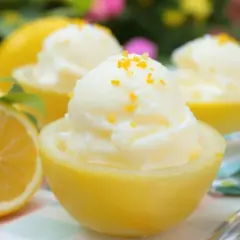 Trois coupes de citron givré, garnies de zestes d'orange, présentées dans des moitiés de citrons évidés. Un citron frais est visible à gauche.