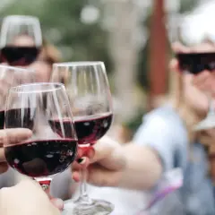 Des mains portent des verres remplis de vin rouge pour une dégustation conviviale en plein air.