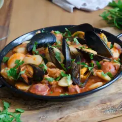 Un plat de moules au chorizo, garni de persil frais, servi dans une poêle noire sur une planche en bois.