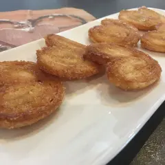 Une assiette blanche présente plusieurs palmiers croustillants, parfaits pour une recette facile.