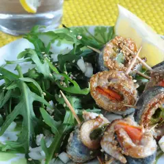 Rouleaux de sardines à la plancha, enrobés de sésame, servis avec une salade verte et un quartier de citron.