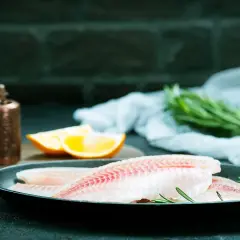 Filets de poisson crus dans une poêle, prêts pour un maquereau au vin blanc. Oranges et romarin à proximité.