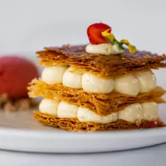 Un délicieux millefeuille croustillant, garni de crème onctueuse et d'une fraise, servi avec une boule de sorbet rouge.