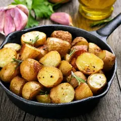 Poêlée de pommes de terre sautées dorées et croustillantes, garnies de romarin frais, avec de l'ail et de l'huile d'olive en arrière-plan.